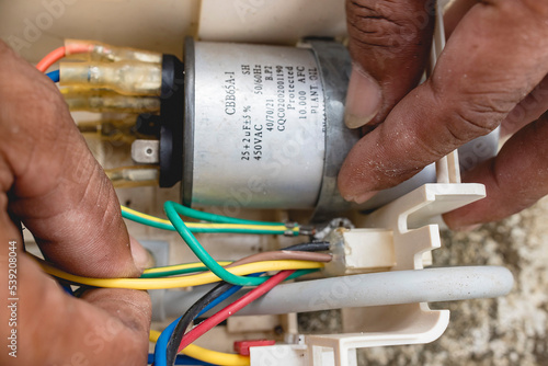 фотографія An electrician examines the wiring connected to CBB65A-1 capacitor inside a window type air conditioner control panel outside