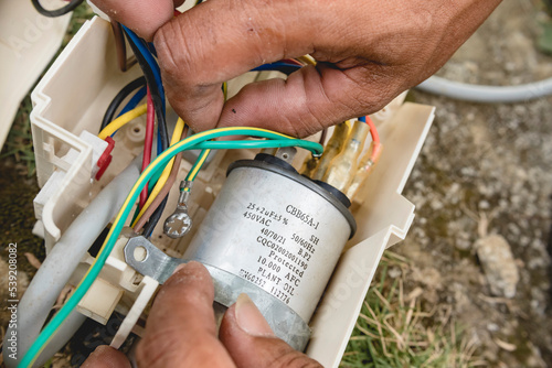 Fotografie An electrician inspects the wiring connected to CBB65A-1 capacitor inside a window type air conditioner control panel outside