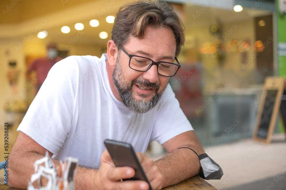 Handsome caucasian man sitting at a cafe table showing something in his mobile phone to his table neighbor Handsome caucasian man sitting at a cafe table showing something in his mobile phone to his table neighbor