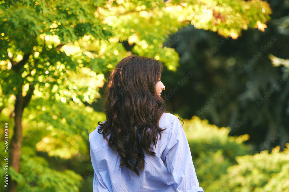 Outdoor portrait of happy young woman enjoying environment in green park, back view Outdoor portrait of happy young woman enjoying environment in green park, back view