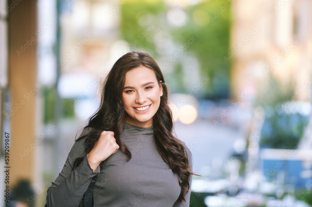 Outdoor portrait of happy young woman posing in the street, holding backpack