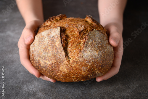 Loaf of freshly baked bread in child hands. Artisan bread on brown background.