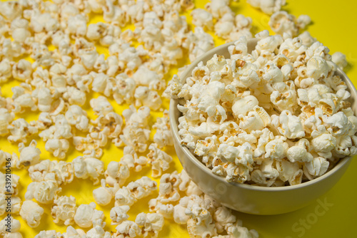 A plate full of popcorn on a yellow background. Delicious salty popcorn