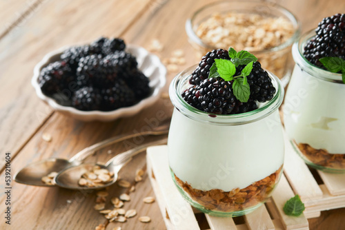 Yogurt with granola, blackberry berry fruits and muesli served in glass jar on wooden background. Healthy breakfast concept. Healthy food for breakfast, top view