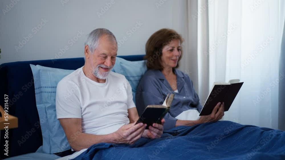 Happy senior couple reading books together in their bed. Happy senior couple reading books together in their bed.