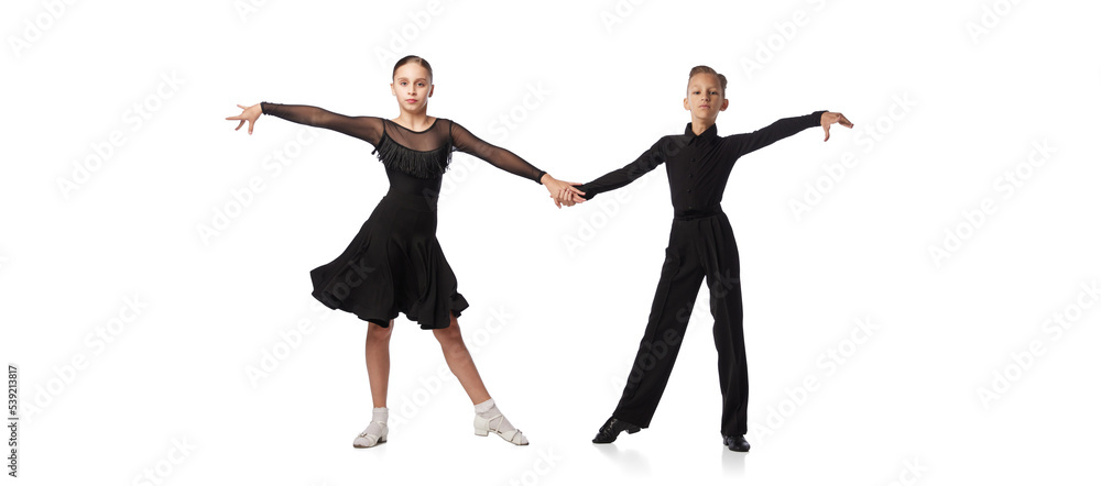 Two kids, school age girl and boy in black stage costumes dancing ballroom dance isolated on white background. Art, sport dance, music, studying