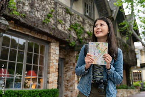 smiling asian Japanese girl visitor holding map and looking at space in Carmel by the sea. she is fascinated by the charming house buildings with creeping plants in the scenic town