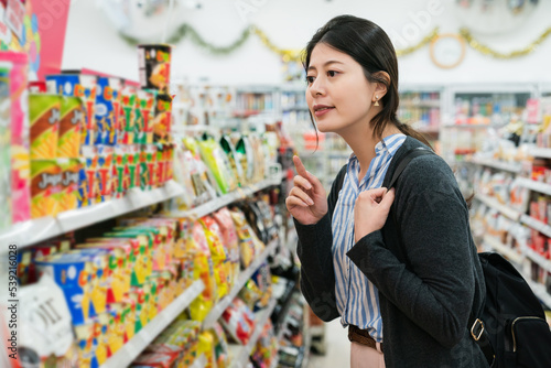 happy asian Japanese girl customer looking at collection of snack food on rack while deciding which to buy in a convenience store in Osaka japan