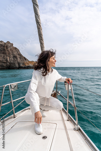 A woman sits on the bow of a yacht on a sunny summer day, the breeze develops her hair, a beautiful sea is in the background