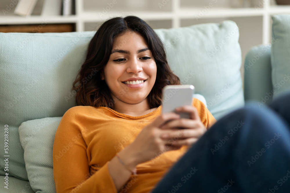 Smiling Young Arab Woman Messaging On Mobile Phone While Relaxing At Home Smiling Young Arab Woman Messaging On Mobile Phone While Relaxing At Home