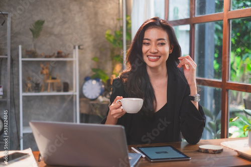 An asian female freelance or Businesswoman is smiling while holding a cup of coffee with cheerful, enjoy, laughing, motivation and happy feeling. An achitect work in cafes.  photo