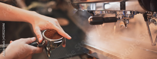 Fotografiet Close up of a hand holding a filter holder with ground coffee and espresso machine or coffee machine with stream and smoke