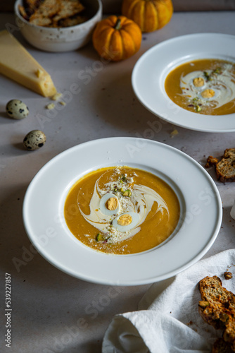 Homemade pumpkin cream soup with quail eggs, parmesan , sour cream and pistachios and biscotti with dried tomatoes and pistachios on white background 