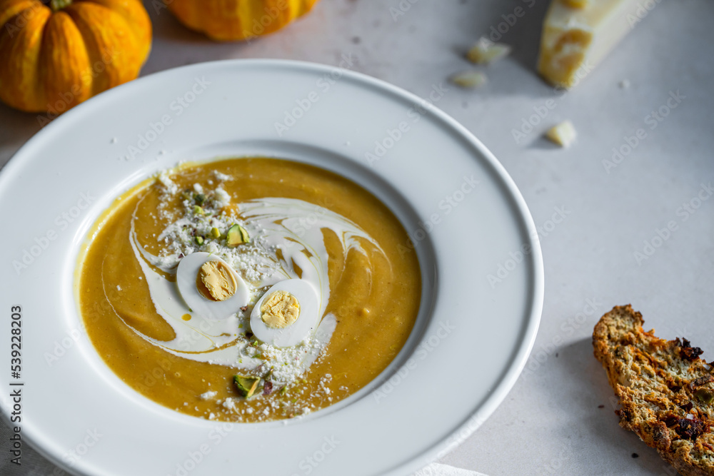 Homemade pumpkin cream soup with quail eggs, parmesan , sour cream and pistachios and biscotti with dried tomatoes and pistachios on white background Homemade pumpkin cream soup with quail eggs, parmesan , sour cream and pistachios and biscotti with dried tomatoes and pistachios on white background