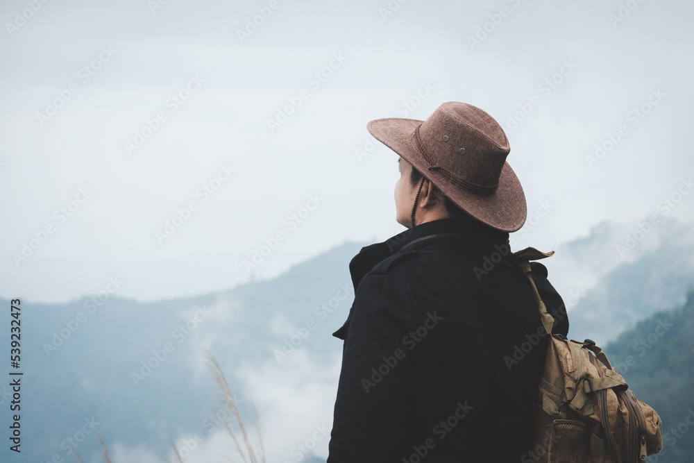 A male traveler in a backpack stands at the top of the mountain  on a foggy and rainy day.Adventure and Success Travel Ideas