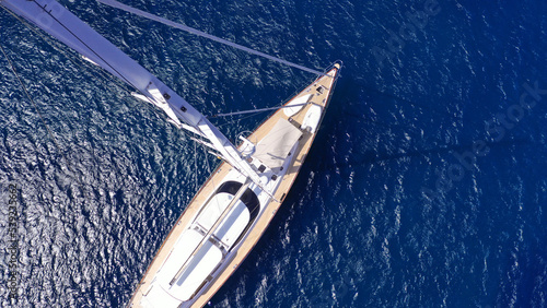 Aerial drone top down photo as seen from top of mast of beautiful sail boat with wooden deck anchored in deep blue Aegean sea