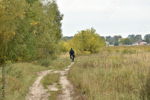 Autumn natural landscape, a man rides a bicycle along a rural road.