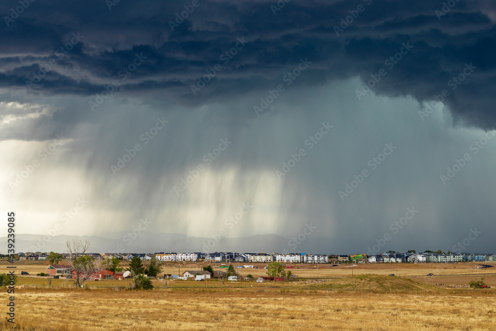 Dark storm clouds over the horizon with heavy rain on a windswept prairie and residential houses in the distance