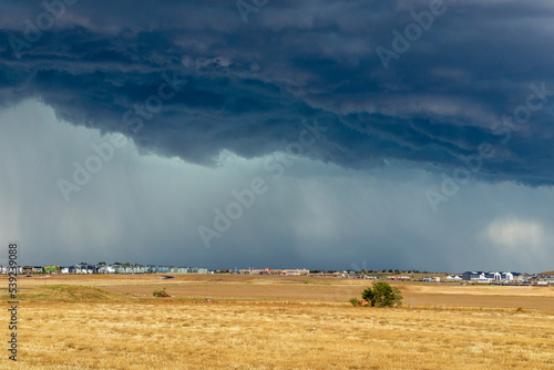 Dark storm clouds over the horizon with heavy rain on a windswept prairie and residential houses in the distance