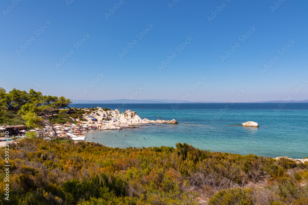 Scenic view on Karydi Beach tourist beach in Vourvourou, Greek peninsula Sithonia, Chalkidiki (Halkidiki), Greece, Europe. Summer vacation at Aegean Mediterranean Sea. Swimming in tropical blue lagoon