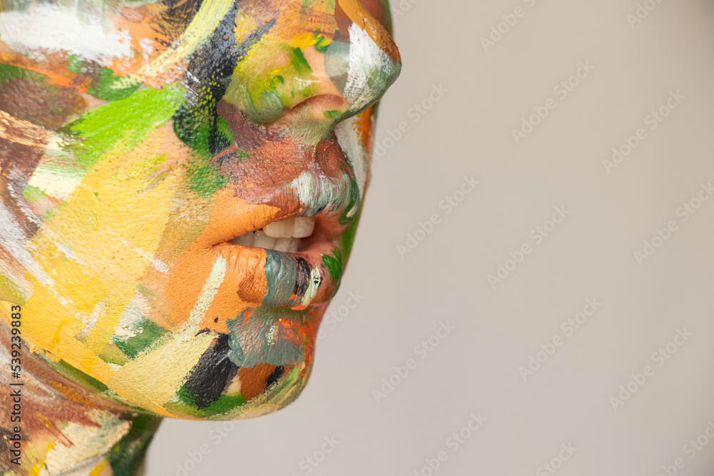 Fototapeta premium The face of a young girl painted with watercolor paint in different colors on an isolated background, creativity, painting on the girl's face