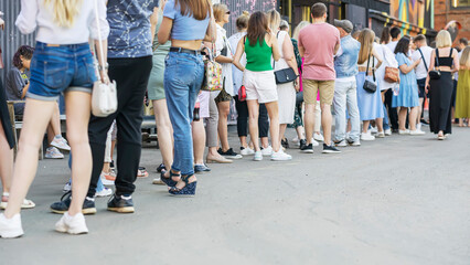 Group of anonymous people queue in line up standing in long line, back view