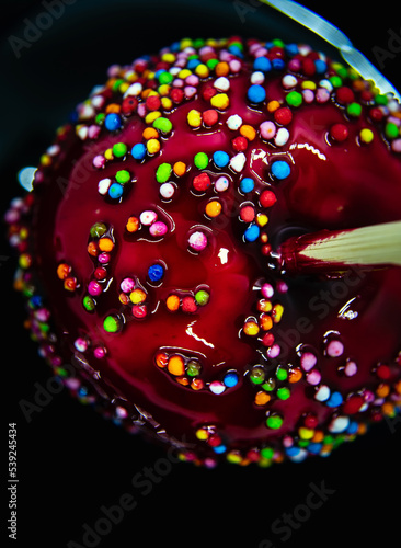 apple on a stick in red caramel with multi-colored icing on a black background