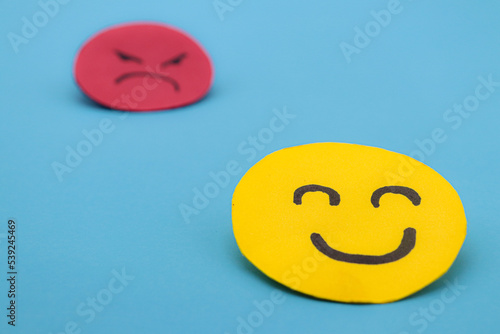 Foto Yellow cut out paper smiley face with another red angry face in the background
