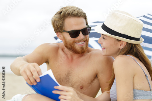 young couple on the beach man reading a book