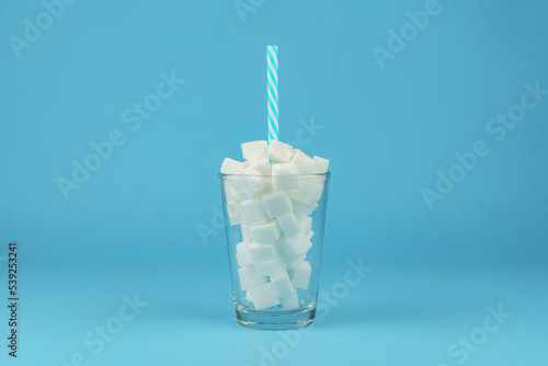 Kubek wypełniony kostkami cukru ze słomką w sirodku na niebieskim tle
