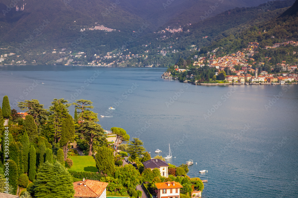 Idyllic Lake Como coastline with village and sailboat at dramatic sunset, Italy