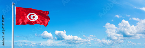 Tunisia flag waving on a blue sky in beautiful clouds - Horizontal banner photo