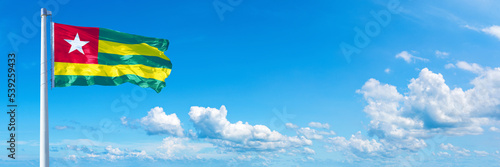 Obraz na płótnie Togo flag waving on a blue sky in beautiful clouds - Horizontal banner