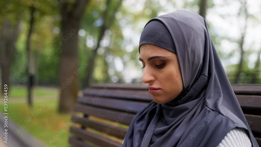 Upset Arab woman in hijab feeling unhappy while sitting on bench in park, stress Upset Arab woman in hijab feeling unhappy while sitting on bench in park, stress