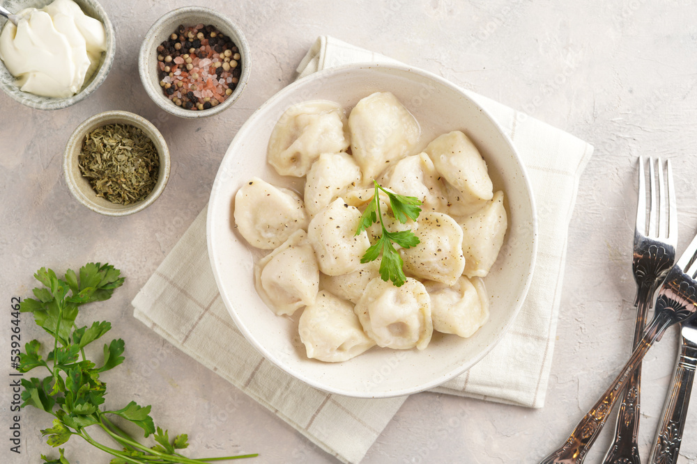 traditional ukrainian east european dish varenyky or chinese wan tan or dim sum - dumplings stuffed with minced meat, fresh cilantro, herbs in white bowl on beige colored kitchen towel. Top view traditional ukrainian east european dish varenyky or chinese wan tan or dim sum - dumplings stuffed with minced meat, fresh cilantro, herbs in white bowl on beige colored kitchen towel. Top view