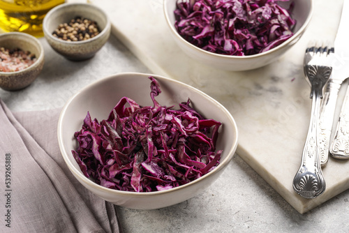 Two salad bowls with german red cabbage chopped in fine stripes on marble board on grey background