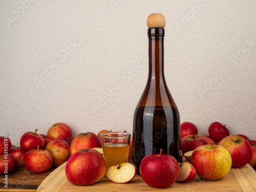Apple cider vinegar in a bottle with apples against a white wall.