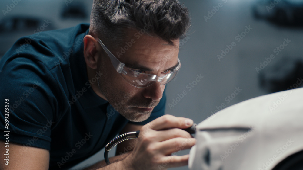 Senior automotive design engineer uses a rotary tool for perfecting the rake sculpture of a car model in a high tech company. Engineer wearing safety goggles works in an automotive company. - obrazy, fototapety, plakaty 