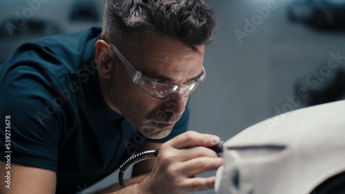 Senior automotive design engineer uses a rotary tool for perfecting the rake sculpture of a car model in a high tech company. Engineer wearing safety goggles works in an automotive company.