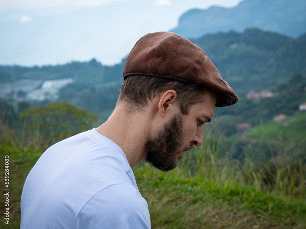 A White Man in a Brown Hat Walks to a Lookout Point to view the Mountains on a Cloudy Day