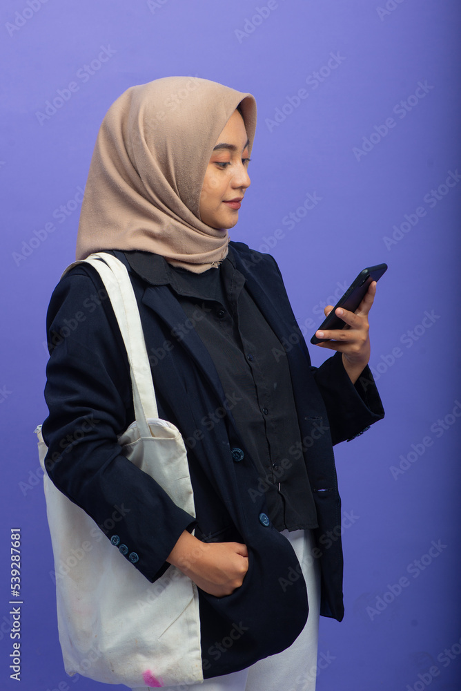 Asian Muslim Woman Holding Mobile Phone, Isolated on Purple Background Asian Muslim Woman Holding Mobile Phone, Isolated on Purple Background
