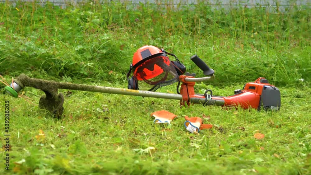 Orange clearing saw, work gloves and protective helmet on green grass, panning video Orange clearing saw, work gloves and protective helmet on green grass, panning video