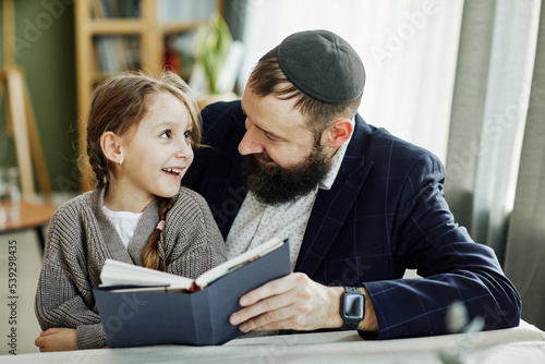 Photo Portrait of smiling jewish father reading book with daughter at home