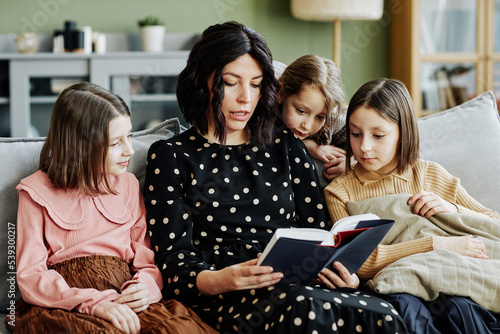 Fototapeta Portrait of young jewish mother reading book to three girls at home