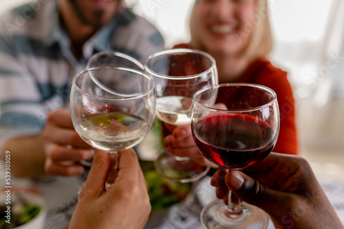 Young cheerful diverse people having lunch together at home. Toasting with Wine. Group of happy friends toasting while eating at the dining table. © lordn