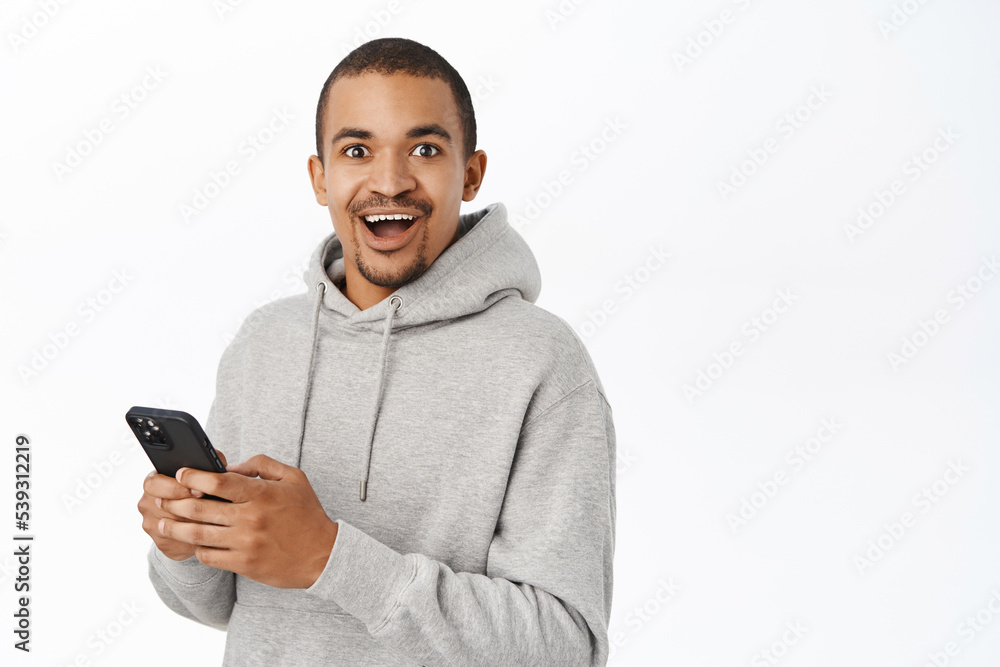 Smiling handsome man using mobile phone, looking at smartphone, standing in casual clothes over white background Smiling handsome man using mobile phone, looking at smartphone, standing in casual clothes over white background
