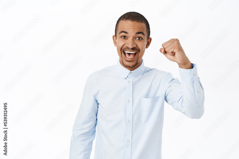 Cheerful arab guy chanting, raising fist up, stay united, smiling happy, standing over white background Cheerful arab guy chanting, raising fist up, stay united, smiling happy, standing over white background