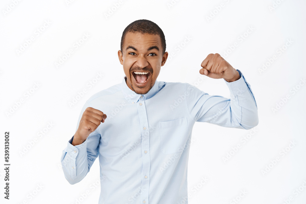 Celebrating success. Excited young man scream of joy, winning and triumphing, feeling like champion, achieve goal, standing over white background Celebrating success. Excited young man scream of joy, winning and triumphing, feeling like champion, achieve goal, standing over white background