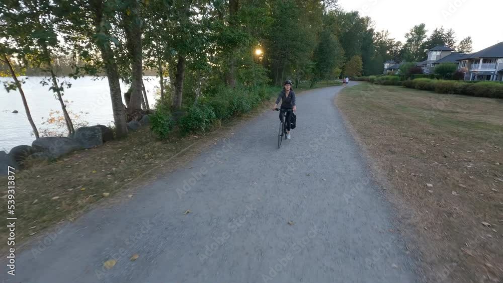 Adventure Woman bike riding on a bicycle trail surrounded by green trees. Summer Sunset. Pitt Meadows, Greater Vancouver, British Columbia, Canada. Adventure Woman bike riding on a bicycle trail surrounded by green trees. Summer Sunset. Pitt Meadows, Greater Vancouver, British Columbia, Canada.