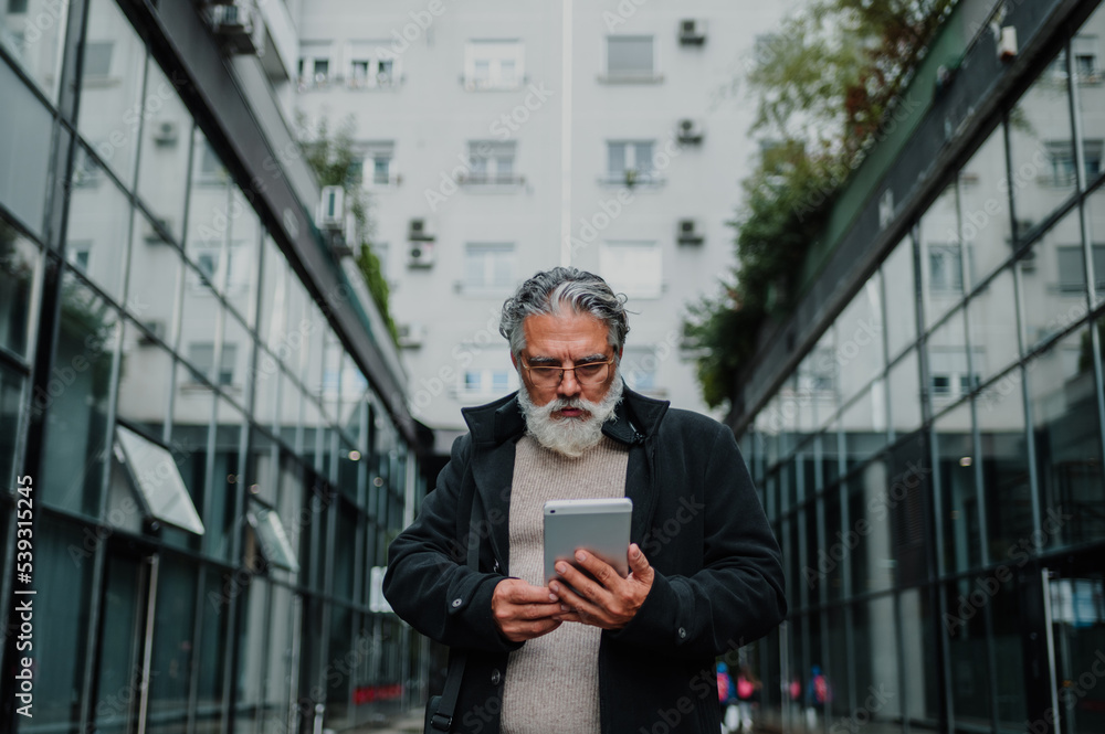 Portrait of a senior businessman using tablet outside of the office building Portrait of a senior businessman using tablet outside of the office building